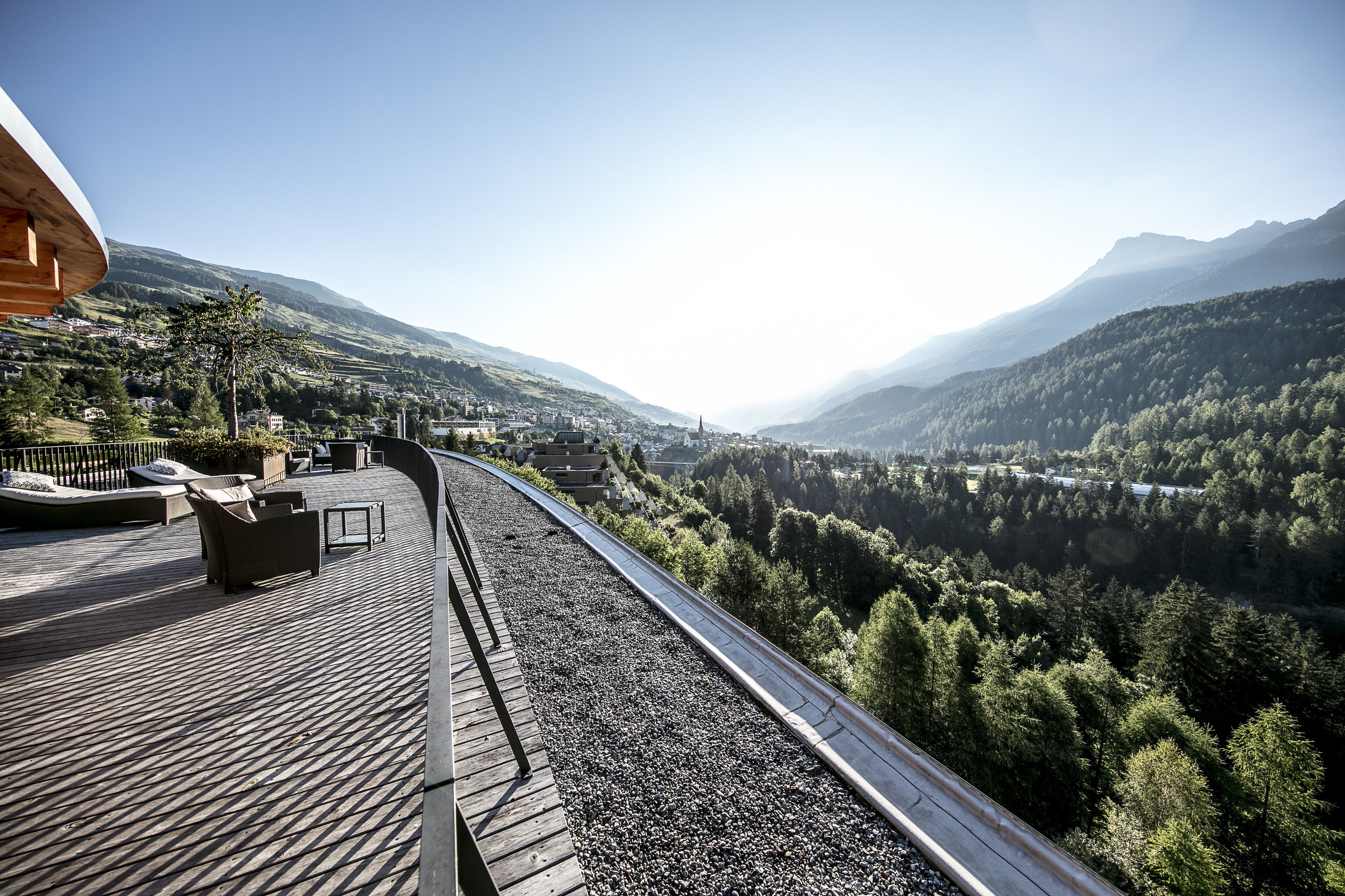 Vías de tren con una terraza de madera y zona de estar con vistas a un paisaje montañoso.