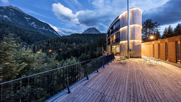 A wooden deck with a railing overlooking a forested mountain area.
