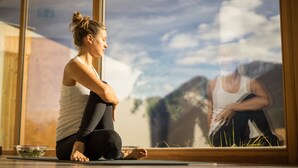 A person sitting on a mat in front of a large window with a view of a building and sky.