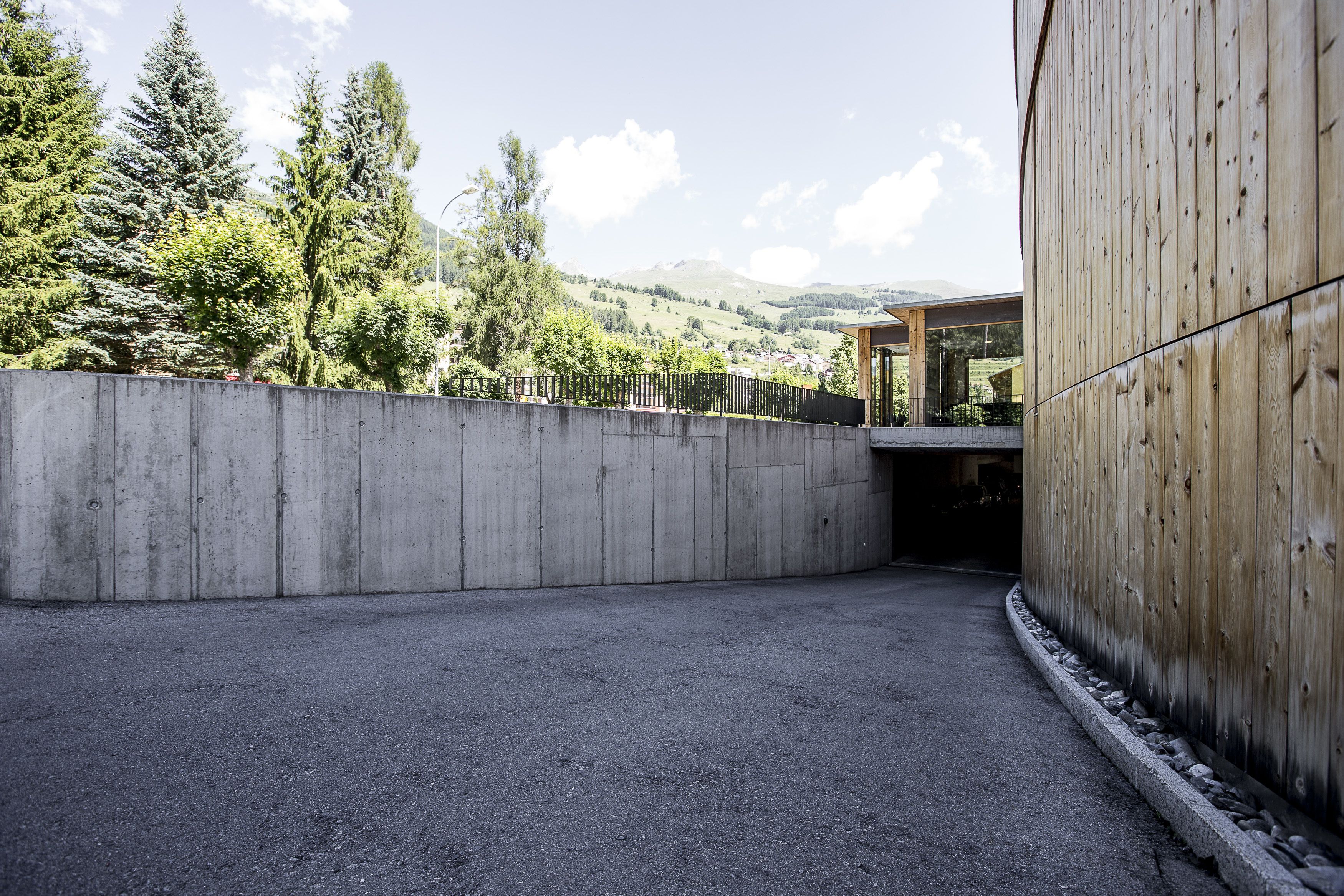 A concrete wall with a wooden fence and a gravel path leading to a building with a wooden facade.
