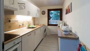Une cuisine avec un plan de travail en bois, un lave-linge, un évier et une fenêtre donnant sur les arbres.