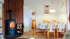 Un salon chaleureux avec un poêle à bois, un coin repas avec des chaises et une table en bois, et une horloge au mur.