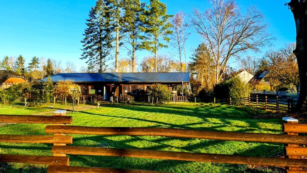 Une clôture en bois rustique, un espace extérieur aménagé avec un toit, et un bâtiment avec un toit bleu.