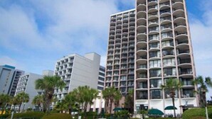 A high-rise hotel with multiple balconies, surrounded by greenery and palm trees. - Rare Two-Story Oceanfront Penthouse • 5 Balconies • Stunning Beach Views (Myrtle Beach)
