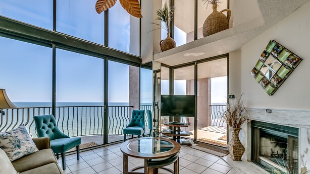 A spacious living area with a large glass balcony, a fireplace, and a television. - Rare Two-Story Oceanfront Penthouse • 5 Balconies • Stunning Beach Views (Myrtle Beach)