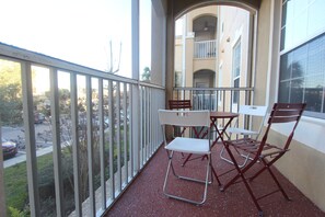 A balcony with a table and chairs, a railing, and a view of a building and street.