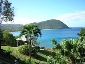 A coastal view with a mountain, a beach, and a structure with a roof. - Cottage with garden, 2 steps from the sea, for 5 people, fully equipped.  (DESHAIES)