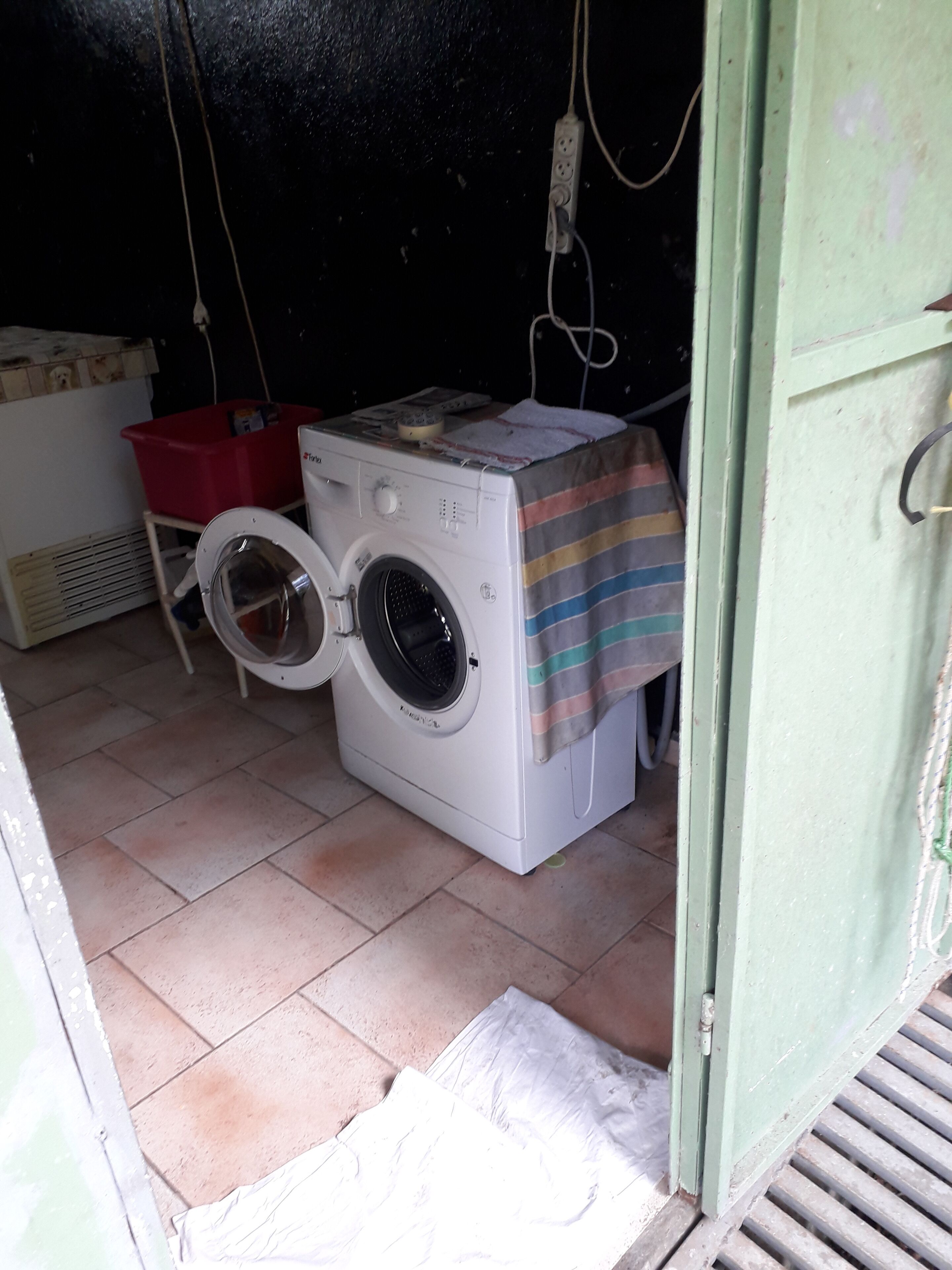 A compact laundry area with a washing machine, a red plastic bin, and a striped cloth on the washing machine.