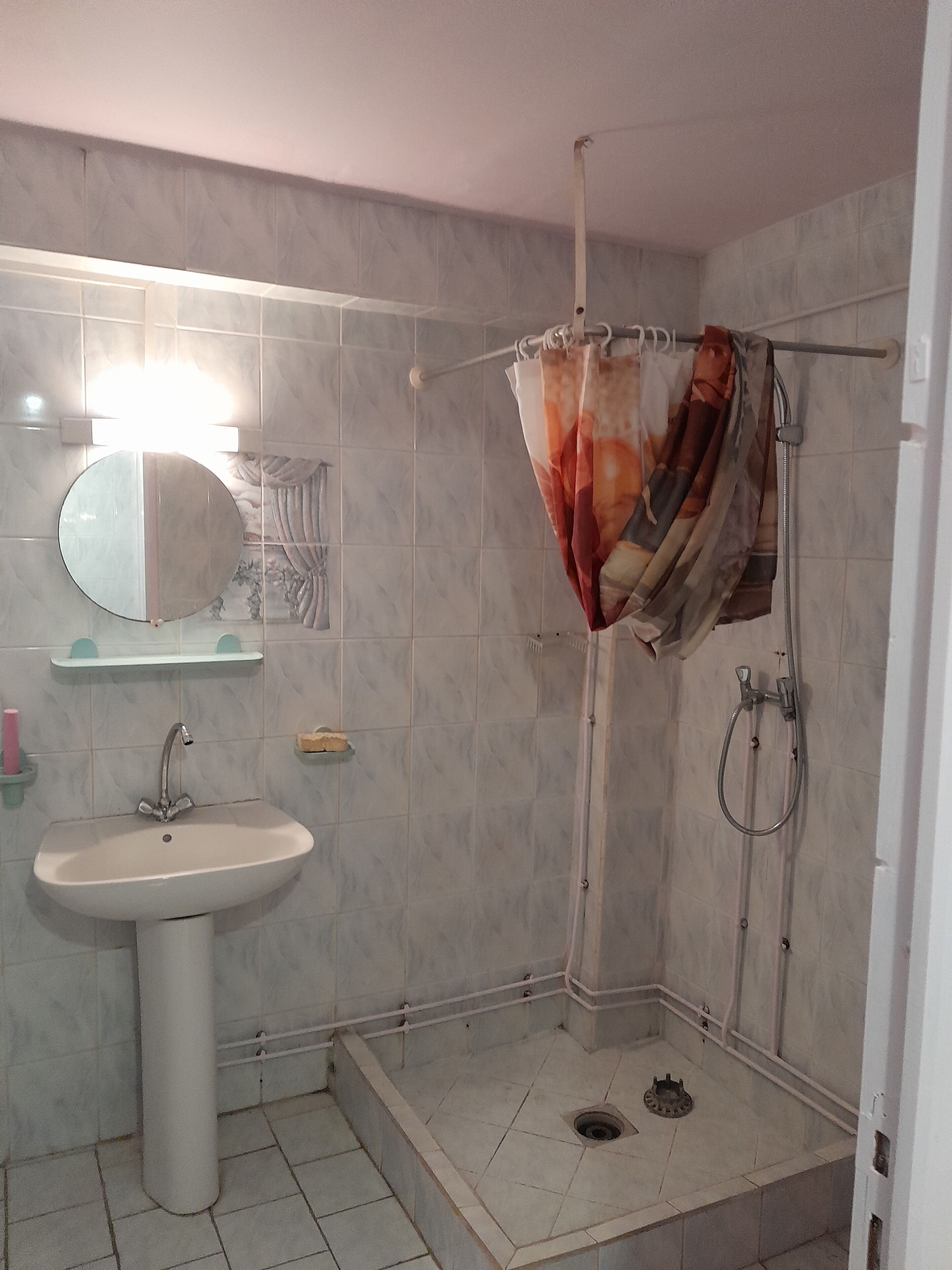 A bathroom with a pedestal sink, a shower with a curtain, and a wall-mounted mirror.