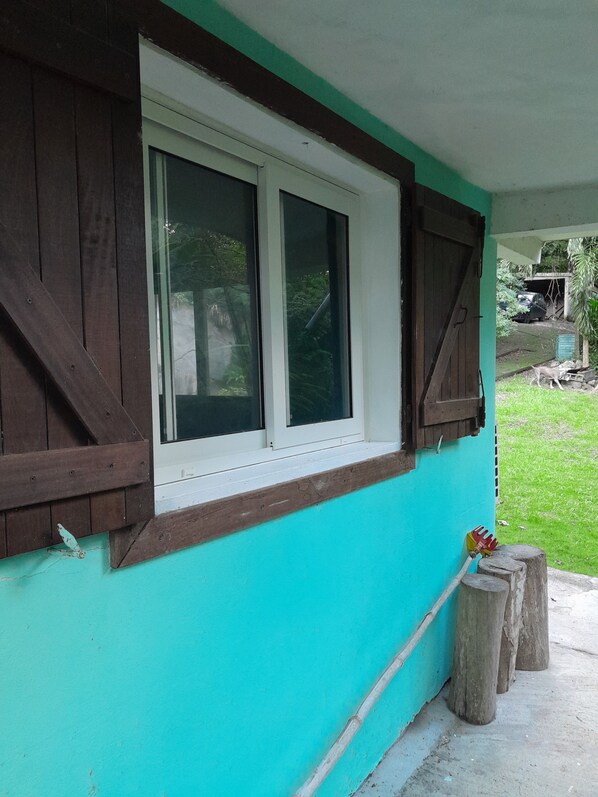 A house with a turquoise exterior, a white window with brown shutters, and a wooden fence. - Cottage with garden, 2 steps from the sea, for 5 people, fully equipped. (DESHAIES)