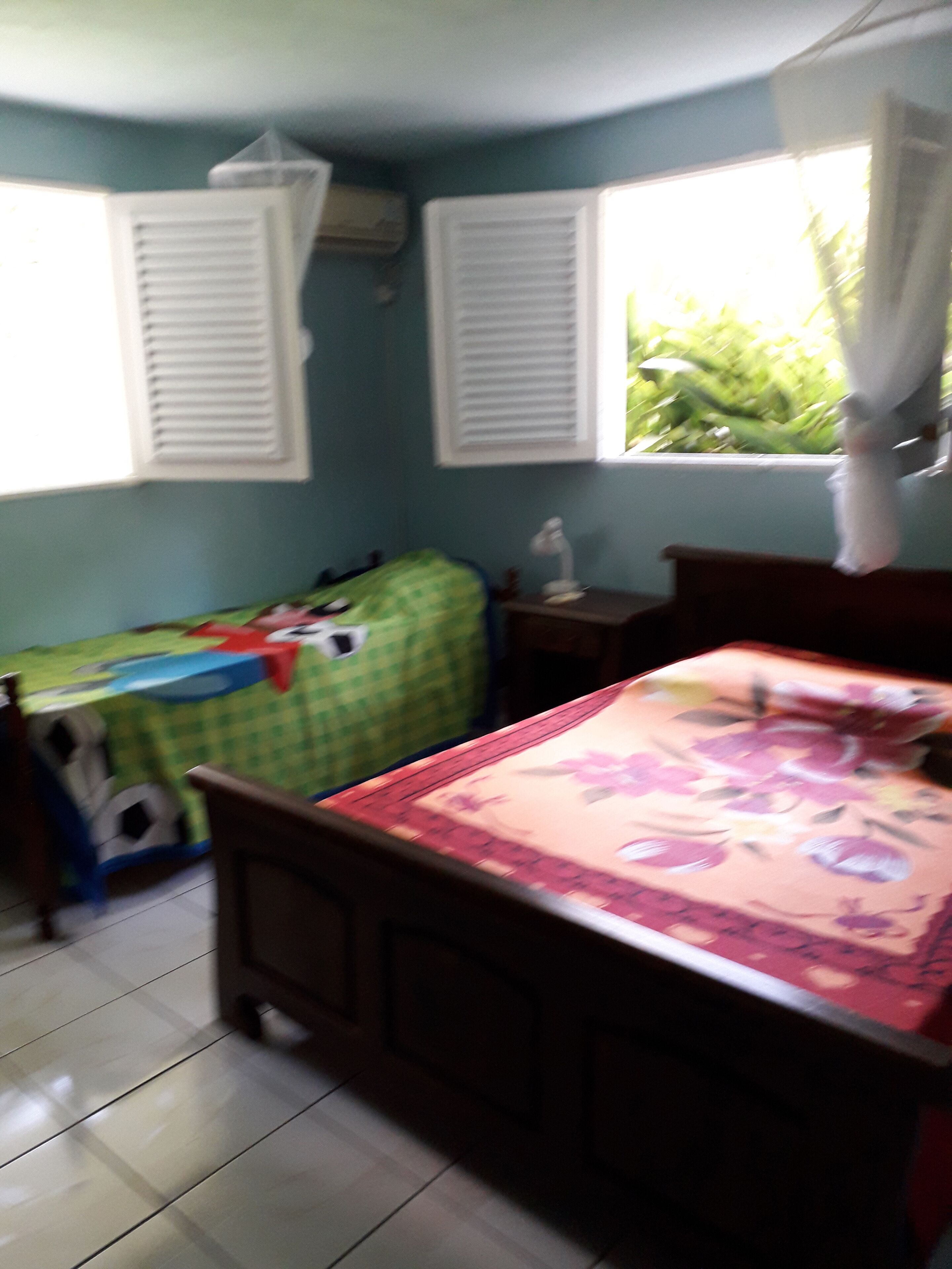 A bedroom with a bed, a small table, and a window with shutters.