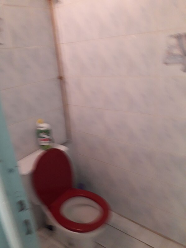 A bathroom with a white toilet and a red seat, a white wall, and a blue door. - Cottage with garden, 2 steps from the sea, for 5 people, fully equipped. (DESHAIES)