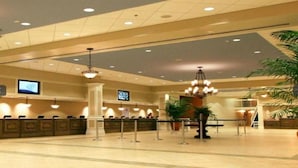 A spacious lobby with a reception desk, multiple chandeliers, and a large potted plant.