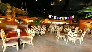 A restaurant with booths and round tables, a bar area, and a ceiling with hanging decorations.