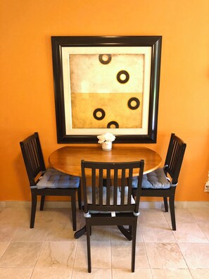 A dining area with a round table, four chairs, and a framed artwork on the wall.