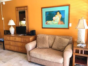 A living room with a sofa, a wooden dresser, a framed painting, a lamp, and a television.