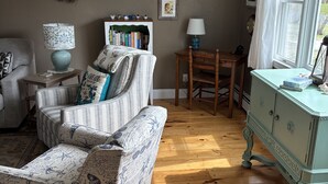 Ein gemütliches Wohnzimmer mit einem gestreiften Sofa, einem kleinen Beistelltisch, einem Bücherregal und einer Wandverzierungen.