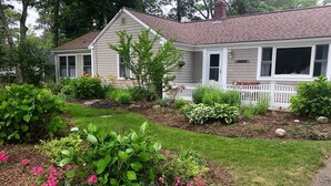 Ein Bungalow mit Veranda, umgeben von einem gepflegten Garten mit verschiedenen Pflanzen und Blumen.