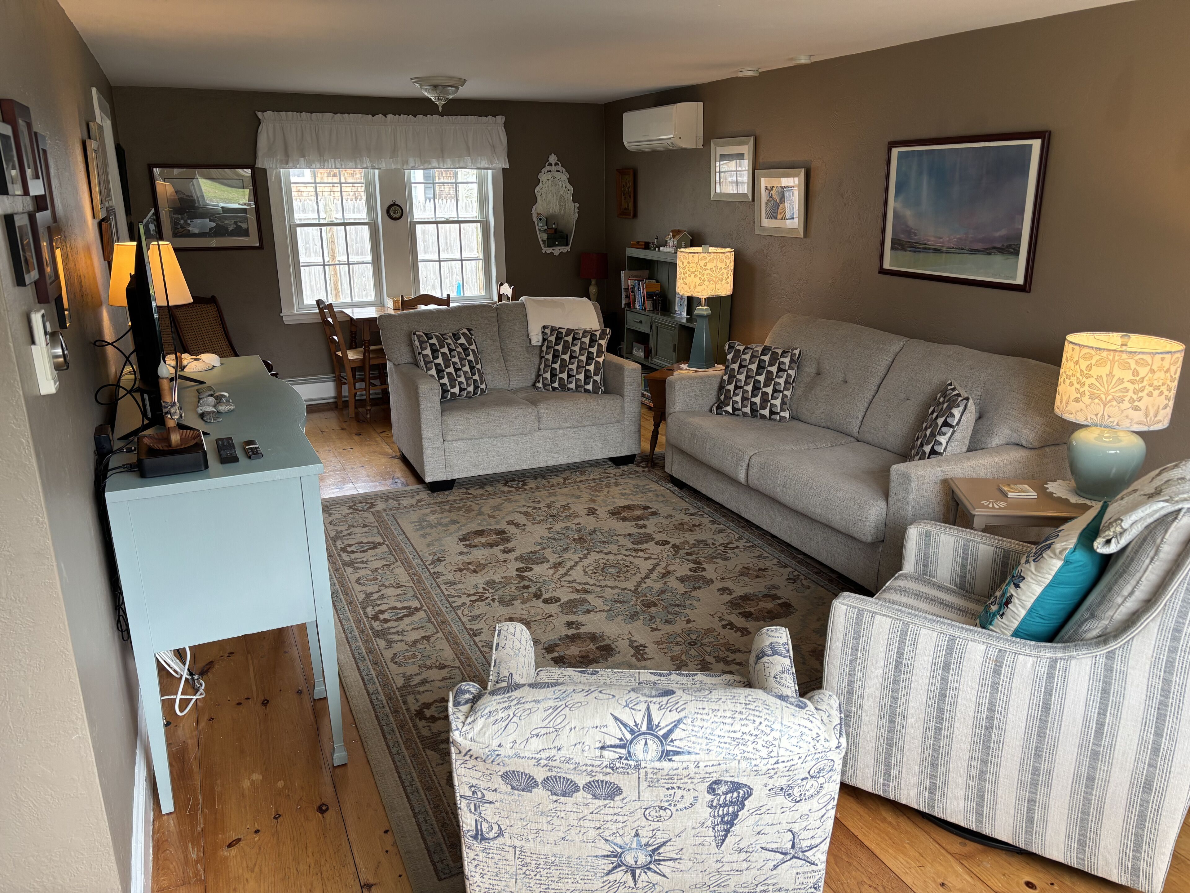 A living room with a sofa, armchairs, a coffee table, a rug, and a desk with a lamp.