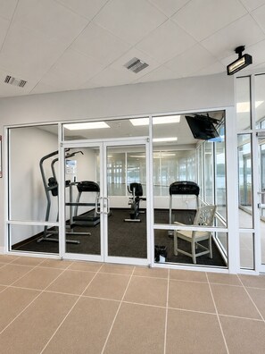 Een sportschool met trainingsapparatuur, glazen deuren en een betegelde vloer.