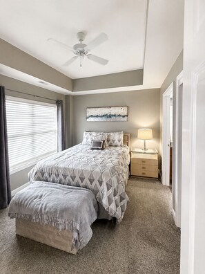 A bedroom with a bed, a nightstand, a lamp, a ceiling fan, and a window with blinds.