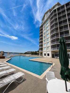 A hotel pool area with multiple lounge chairs and a large building with balconies.