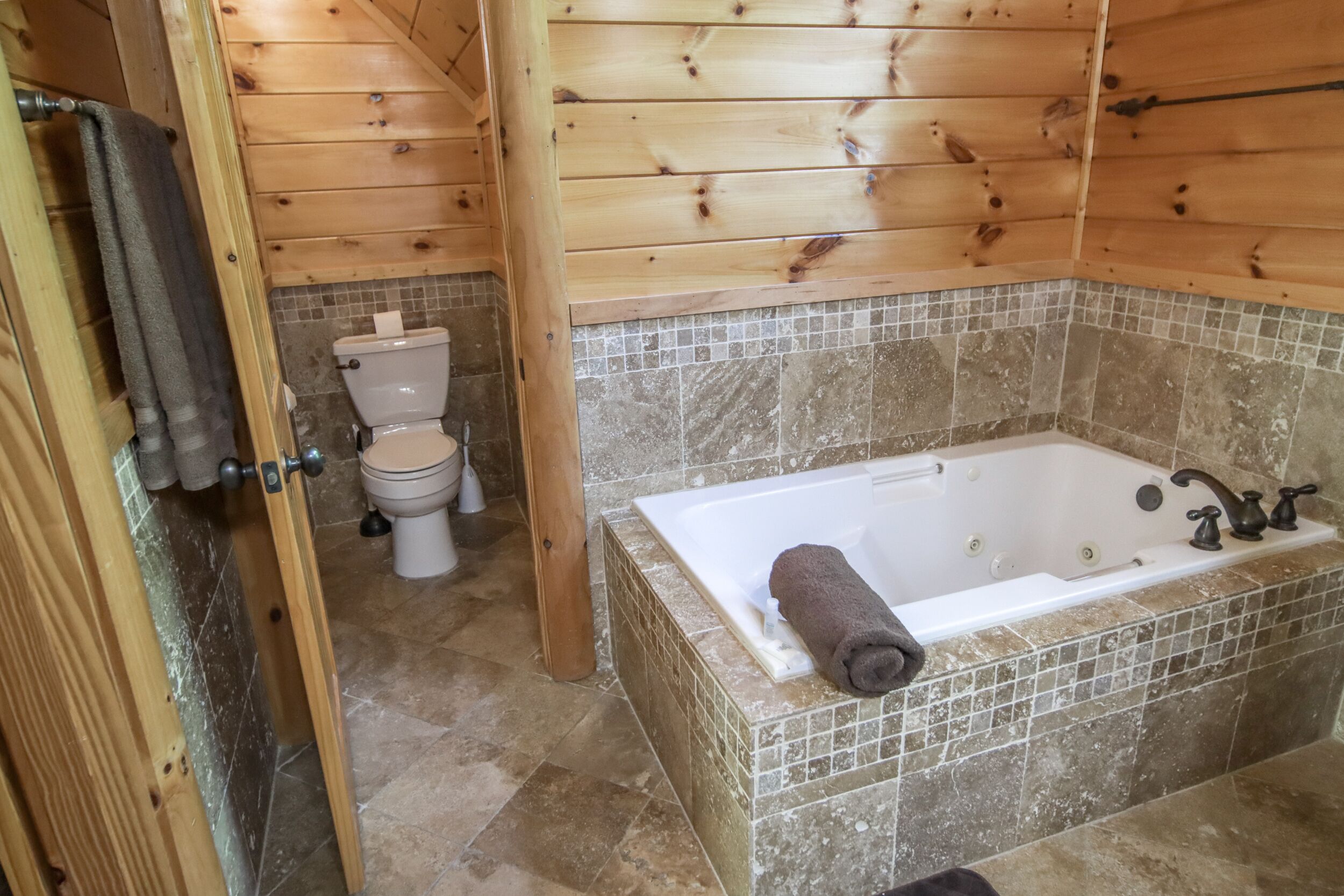 A wooden-paneled bathroom with a white bathtub, a toilet, and a shower area.