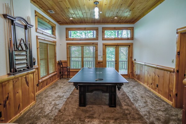 A ping pong table in a room with wooden paneling, large windows, and a ceiling light fixture.
