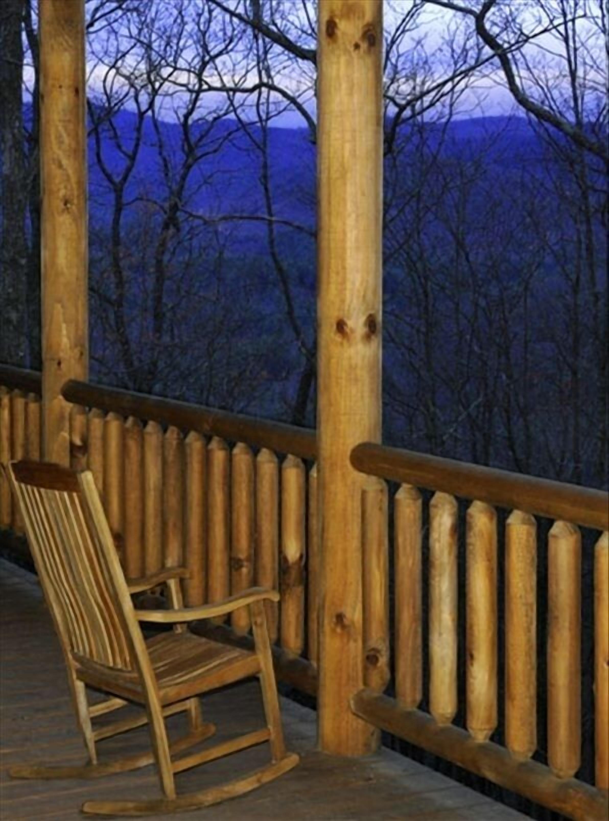 A wooden deck with a wooden chair and a railing overlooking a mountainous landscape.