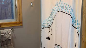 Un baño con cortina de ducha con estampado de lluvia, un perchero con toalla y una ventana con persianas.