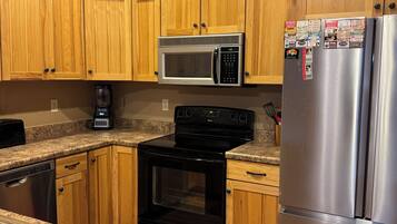 Una cocina con armarios de madera, un refrigerador de acero inoxidable, un microondas, un horno y una cafetera.