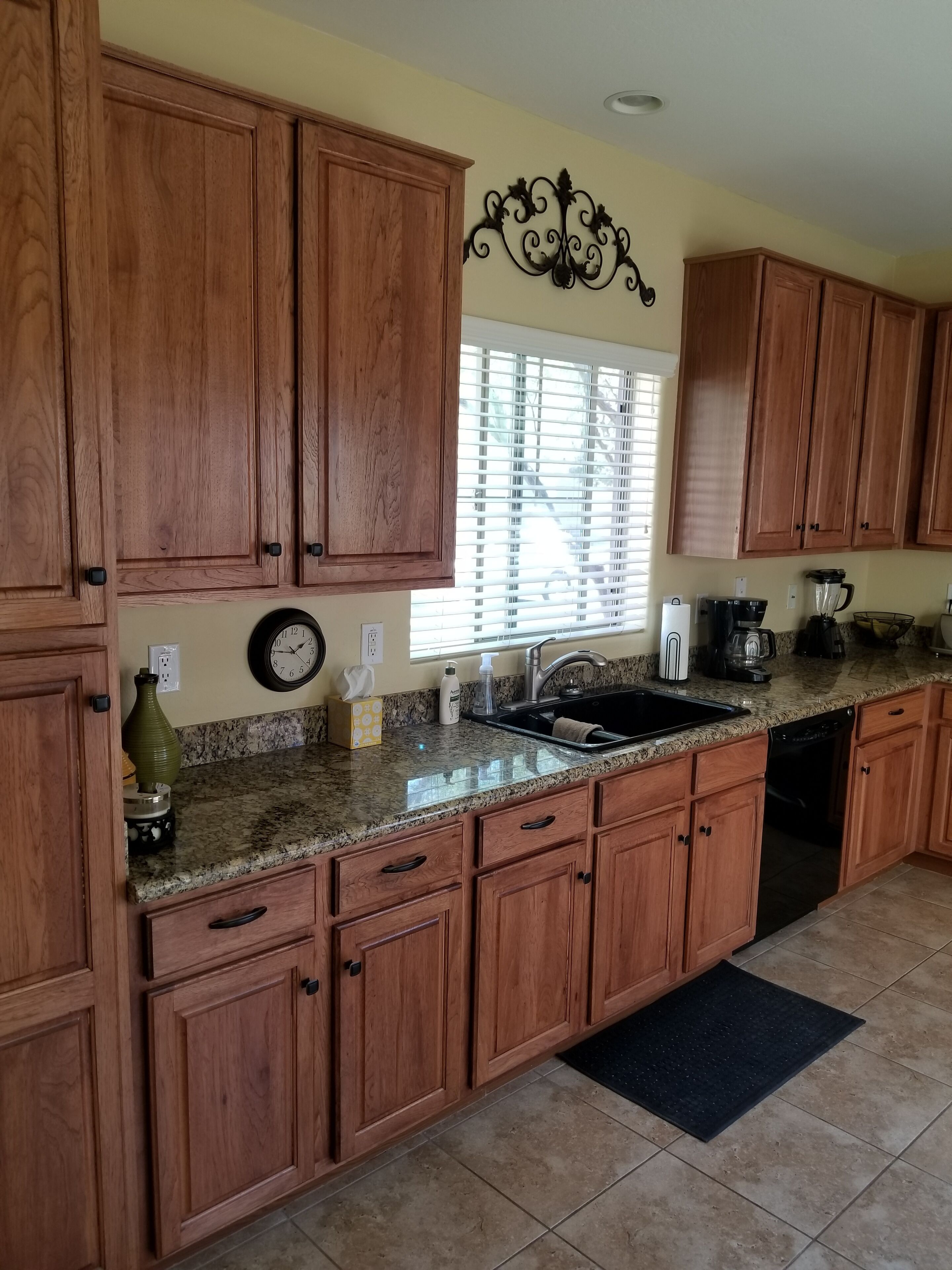 A kitchen with wooden cabinets, granite countertops, a sink, and a window with blinds.