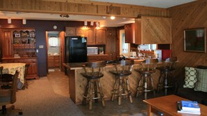 A kitchen with wooden cabinets, a black refrigerator, a microwave, and a sink. There are four stools around the bar area. - The Bunkalow Lakefront Compound w Lifts for your Speed Boat & Tritoon (Ludington)