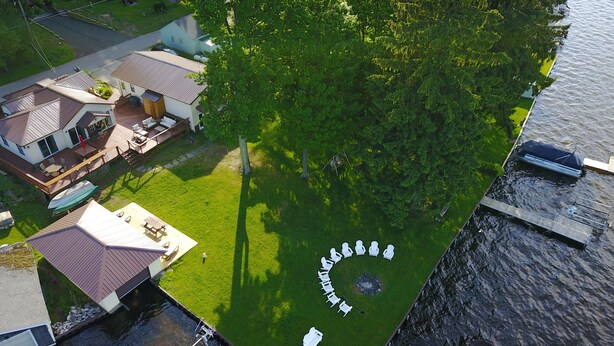 An aerial view of a property with a circular arrangement of white chairs on a grassy area, a dock, and a house with a deck. - The Bunkalow Lakefront Compound w Lifts for your Speed Boat & Tritoon (Ludington)