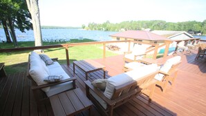 A wooden deck with outdoor furniture, including sofas and chairs, overlooking a lake. - The Bunkalow Lakefront Compound w Lifts for your Speed Boat & Tritoon (Ludington)