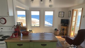 A kitchen with a wooden countertop, a stove, and a dining area with a chair. - Oceanfront Cottage at the Edge of the Earth, St. John's  (Pouch Cove)