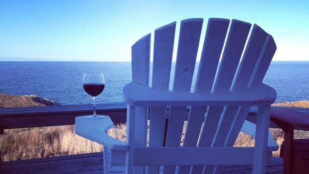 A white Adirondack chair with a glass of red wine on a wooden deck overlooking the ocean. - Oceanfront Cottage at the Edge of the Earth, St. John's  (Pouch Cove)