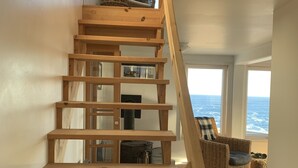 A wooden staircase with a view of the ocean through large windows. - Oceanfront Cottage at the Edge of the Earth, St. John's  (Pouch Cove)