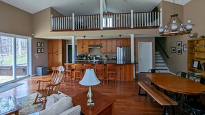 A spacious living area with a high ceiling, a dining table, a kitchen with wooden cabinets, and a staircase leading to an upper level. - Secluded Waterfront Home Located On 82 Private Acres! Close to HH State Park!
 (Laurelville)