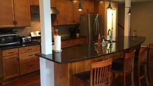 A modern kitchen with wooden cabinets, a stainless steel refrigerator, a microwave, and a gas stove. There are wooden chairs around a central island with a black countertop. - Secluded Waterfront Home Located On 82 Private Acres! Close to HH State Park!
 (Laurelville)
