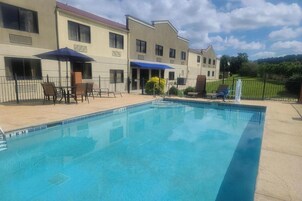 Una piscina con tumbonas y sombrillas, rodeada por un edificio con varias ventanas y una entrada cubierta.