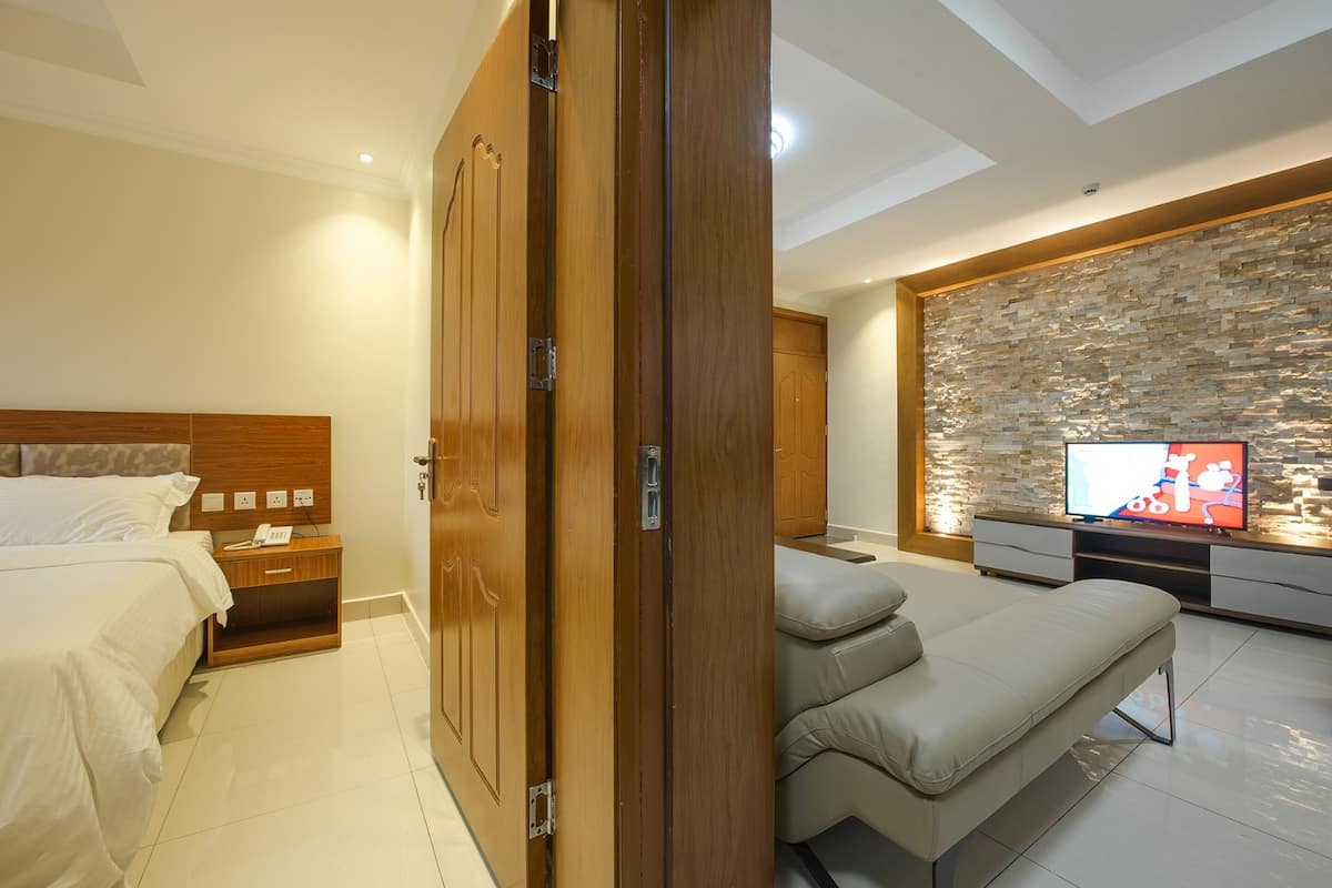 A modern bedroom with a wooden wardrobe, a bed, a TV, and a stone wall.