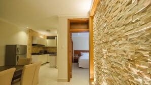 A modern kitchen with a dining area, a stone wall, and a bedroom visible through an open doorway.
