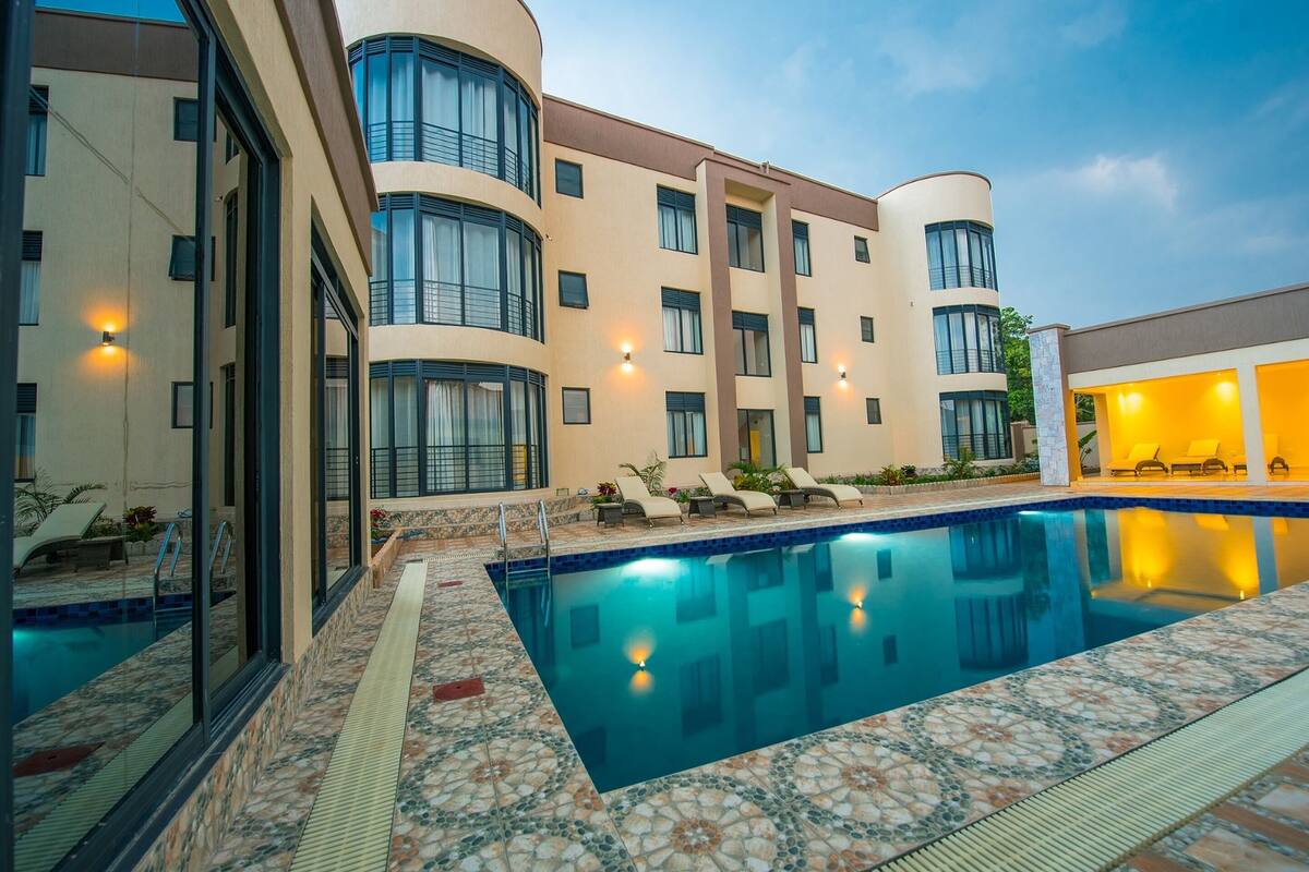 A hotel with a swimming pool, lounge chairs, and a well-lit exterior.