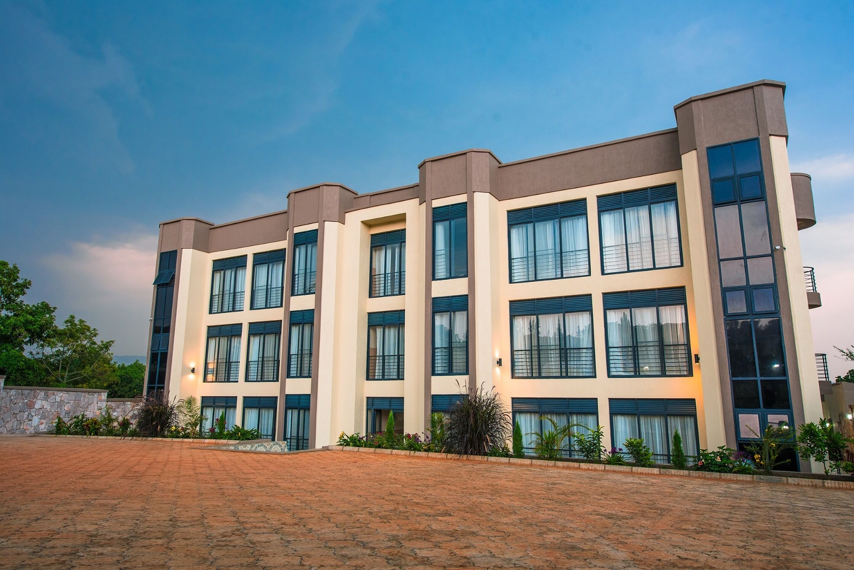 A modern multi-story building with a symmetrical facade, large windows, and a paved courtyard.
