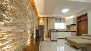 A modern living room with a stone accent wall, a flat-screen TV, a wooden coffee table, and a beige sofa.