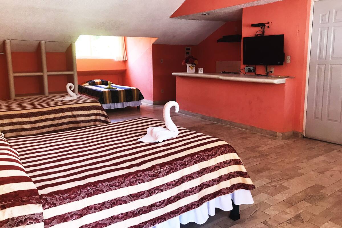Quarto de hotel com duas camas, televisão, uma mesinha e uma janela.