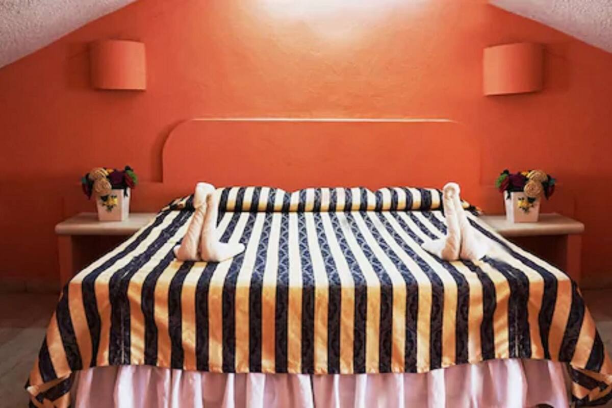 Quarto com colcha listrada, duas mesas de cabeceira com abajures e teto inclinado.
