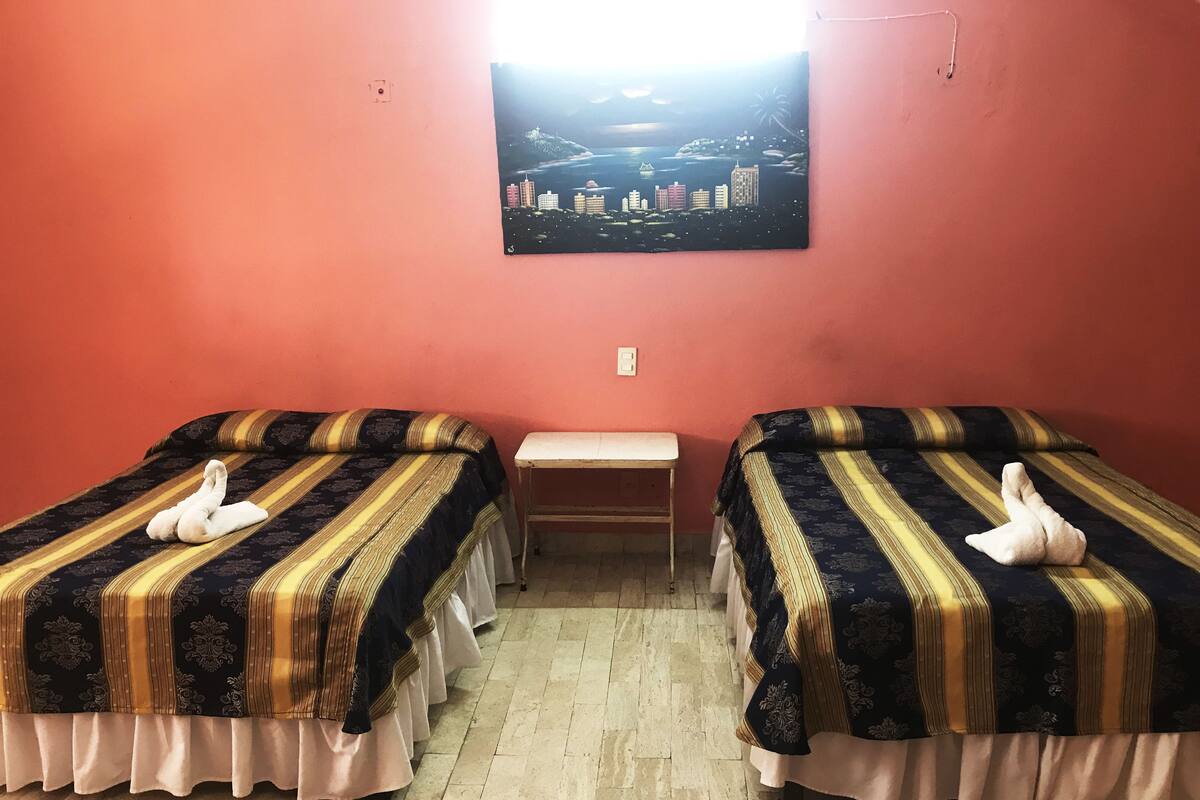 Quarto com duas camas, um banco e um quadro na parede.