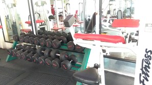Une salle de sport équipée de divers appareils d’exercice, notamment des haltères et des bancs.